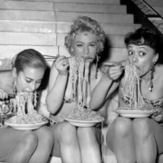 three young 20th century women eating a heavy serving of spaghetti with chopsticks; a big serving is in all their mouths