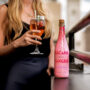 millennial woman holding a glass of Sparkling Rosé cocktail; Bacana Sangria bottle is in front of her